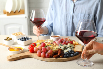 Women holding glasses of wine at light grey table with different snacks indoors, closeup