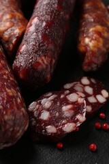 Different smoked sausages and peppercorns on black table, closeup