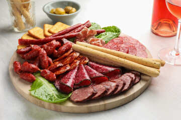 Different smoked sausages and other snacks served with wine on white table, closeup