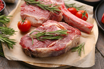 Pieces of raw beef, rosemary and tomatoes on wooden table, closeup