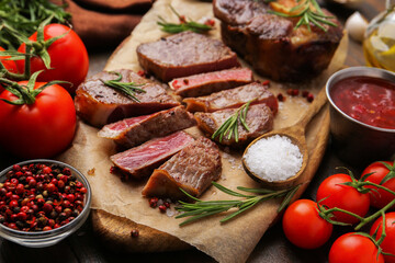 Pieces of delicious beef meat, spices and tomatoes on table, closeup