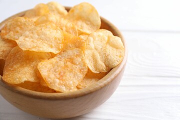 Tasty potato chips in bowl on white wooden table, closeup. Space for text