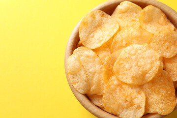 Tasty potato chips in bowl on yellow background, top view. Space for text