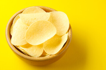 Tasty potato chips in bowl on yellow background, closeup. Space for text