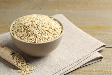 Raw brown rice in bowl and scoop on wooden table, closeup