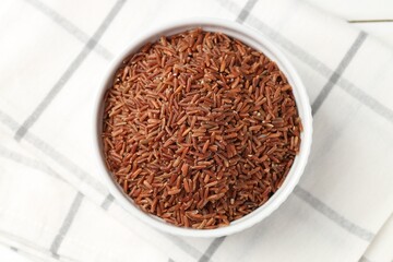 Raw brown rice in bowl on white table, top view
