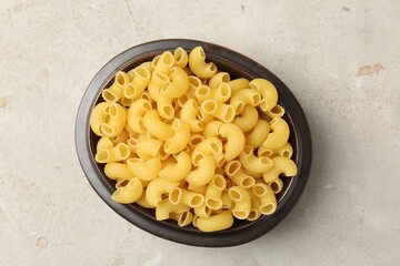 Raw horns pasta in bowl on gray textured table, top view