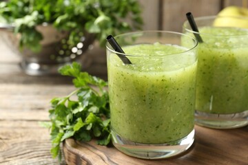 Healthy parsley smoothie in glasses and leaves on wooden table, closeup