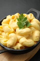 Delicious macaroni and cheese with parsley on black table, closeup