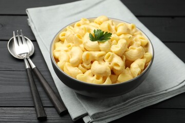 Delicious macaroni and cheese with parsley served on black wooden table, closeup