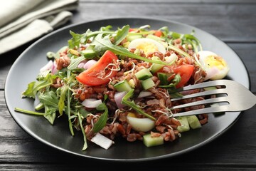 Delicious salad with brown rice on black wooden table, closeup