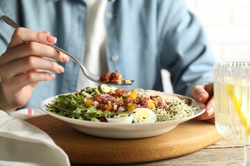 Woman eating delicious salad with brown rice at wooden table, closeup