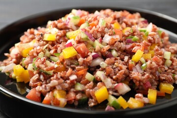 Tasty salad with brown rice on black table, closeup