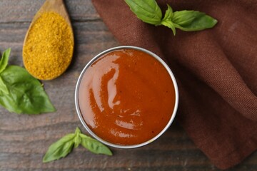 Tasty curry sauce in metal dish, powder and basil on wooden table, flat lay
