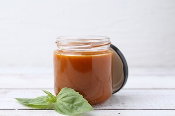 Tasty curry sauce in glass jar and basil on white wooden table, closeup