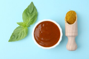 Tasty curry sauce, powder and basil leaves on light blue background, flat lay