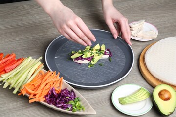 Woman making tasty spring roll at grey wooden table, closeup