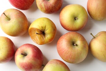 Rotten apple among fresh ones on white wooden table, flat lay