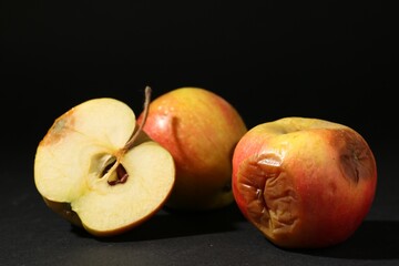 Cut and whole rotten apples on black background, closeup