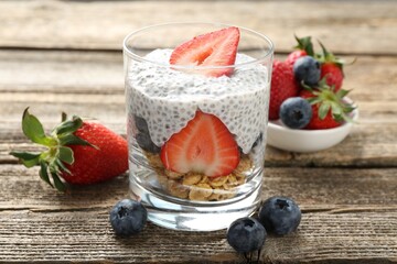 Delicious dessert with chia seeds, yogurt, granola, strawberries and blueberries in glass on wooden table, closeup. Superfood