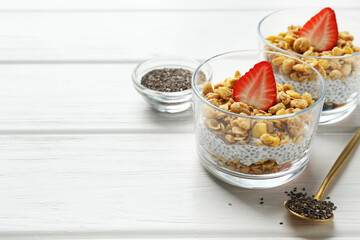 Delicious dessert with chia seeds, yogurt, granola and strawberries in glasses on white wooden table, closeup with space for text. Superfood