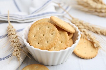 Tasty salty crackers with wheat spikes on white tiled table, closeup