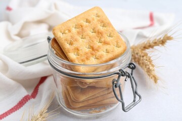 Tasty salty crackers and wheat spikes on white table, closeup