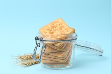 Tasty salty crackers and wheat spikes on light blue background, closeup