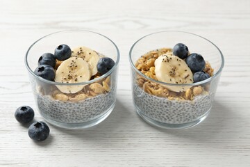 Delicious dessert with chia seeds, yogurt, granola, blueberries and banana on white wooden table, closeup. Superfood