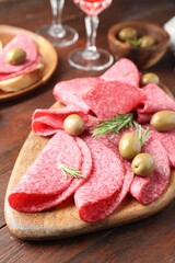 Slices of delicious sausage with olives and rosemary served on wooden table, closeup