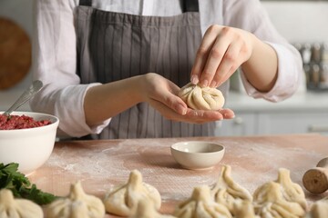 Woman making khinkali on table in kitchen, closeup