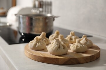 Cooktop with pot and uncooked khinkali on countertop in kitchen, selective focus