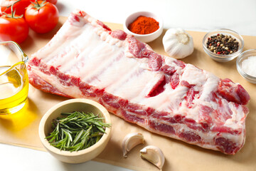 Raw pork ribs, spices and tomatoes on white table, closeup