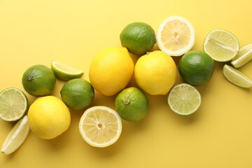 Fresh ripe lemons and limes on yellow background, flat lay