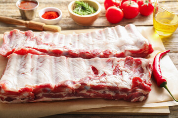 Raw pork ribs, spices and tomatoes on wooden table, closeup