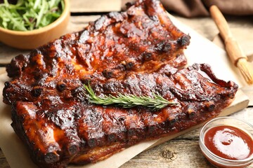 Tasty roasted pork ribs served with rosemary, sauce and salad on wooden table, closeup