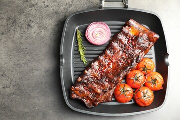 Delicious roasted pork ribs with rosemary, tomatoes and onion on grey table, top view