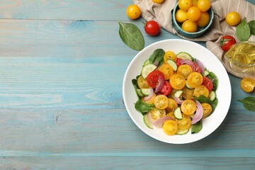 Fresh salad with yellow tomatoes served on light blue wooden table, flat lay. Space for text