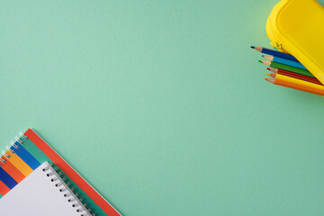 Brightly arranged school supplies including colorful pencils and a notebook presented on a green...
