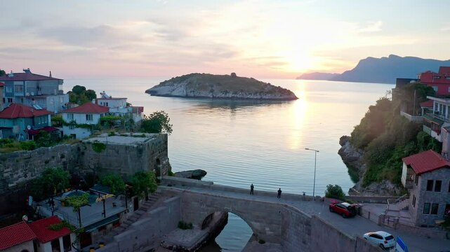 Drone footage moving from the enchanting atmosphere of Amasra at sunset towards Boztepe Island. People are seen on the historical stone bridge.