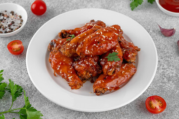 Baked chicken wings in a sweet chili sauce and sesame seeds on a white plate on a concrete background. Top view, copy space.