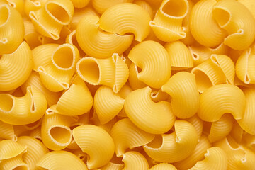 Dry pipe rigate pasta with curved, ribbed shapes in golden yellow, perfect for food background or culinary design use, top view