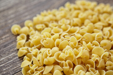 Close-up side view of dry funghetti pasta scattered on a rustic wooden surface, showing curled shapes and ridged texture with soft background blur