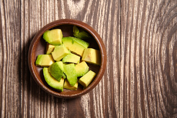 Bowl filled with freshly diced avocado pieces placed on a rustic wood surface, ideal for food...