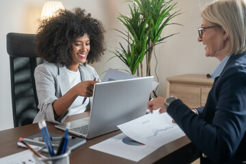 Two beautiful female colleagues interacting while working in office. They are interacting and smiling.