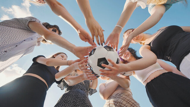 High school girls holding a soccer ball in a circle, representing teamwork and unity during summer vacation