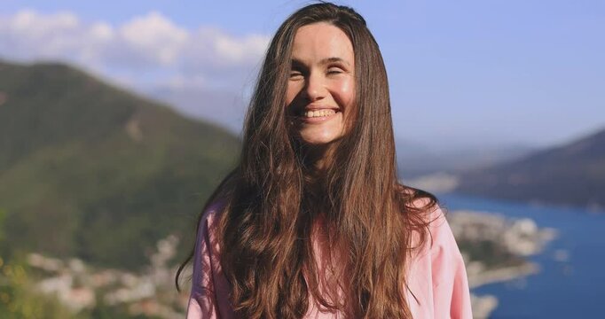 Amazed excited woman hairstyle in pink long sleeves open mouth in surprise looking at camera with big eyes, shocked standing near mountains and sea landscapes. Oh my god wow, yes gesture, win dance.