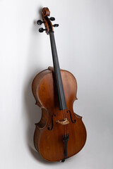 High-resolution studio photograph of a full-size classical cello standing vertically on a clean white background. The image showcases the elegant shape and wooden texture of the string instrument, com