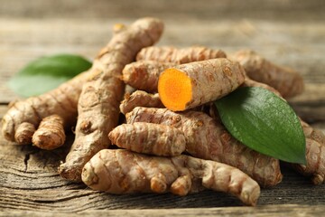 Pile of tumeric rhizomes with leaves on wooden table, closeup
