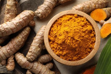 Turmeric powder in bowl and roots on table, flat lay